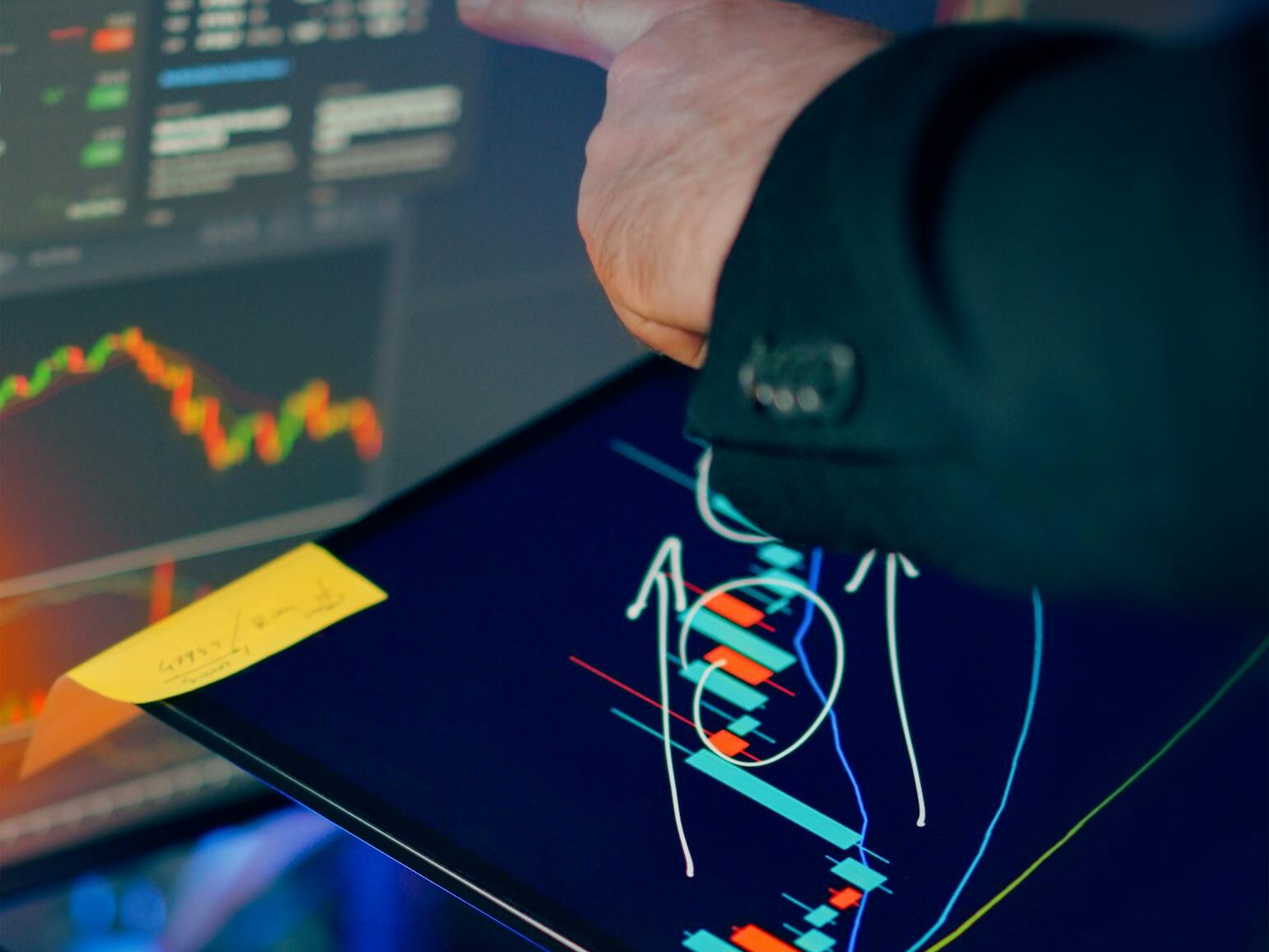 A business professional examines financial charts on a tablet and monitor for investment strategy.