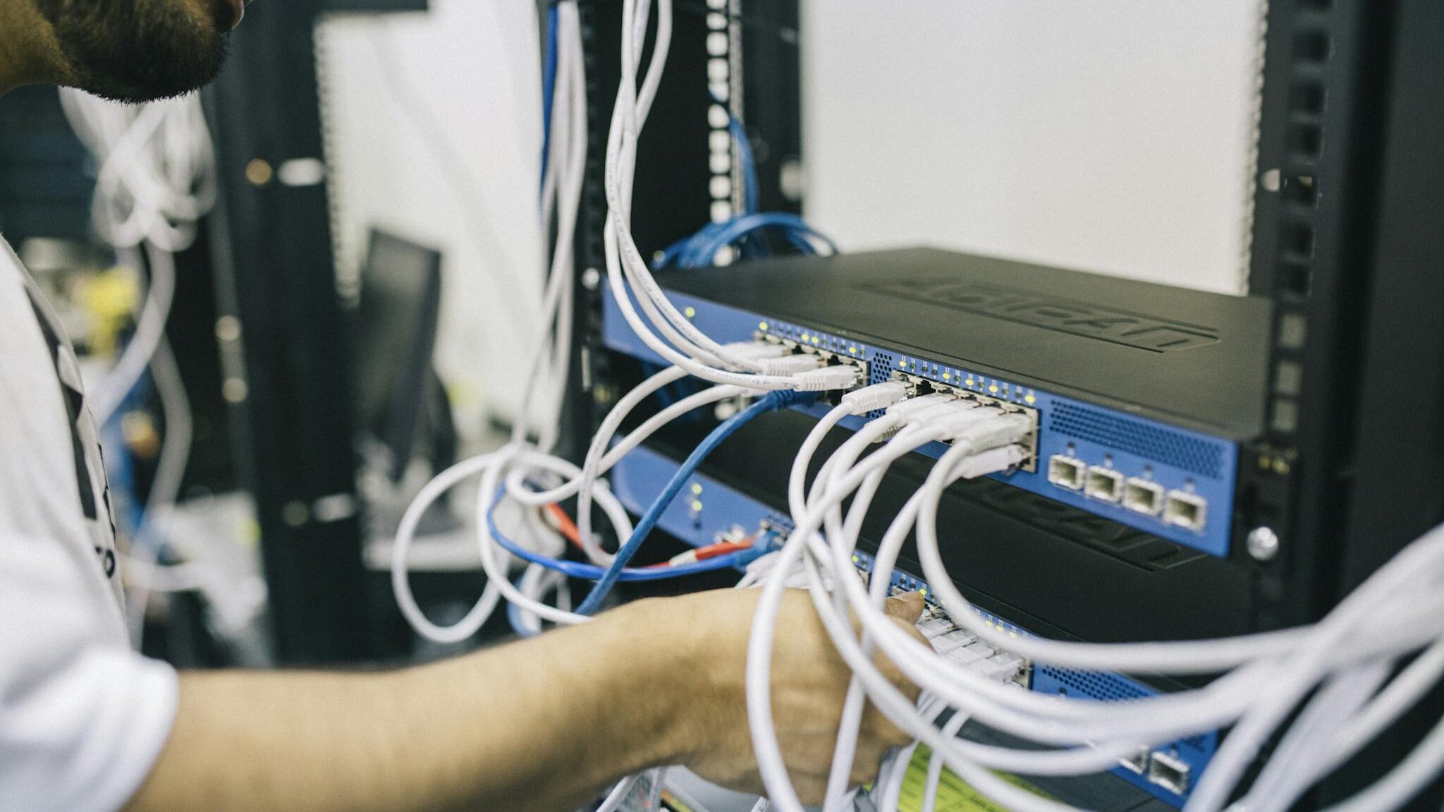 An IT professional configuring network cables in a server rack, focusing on Ethernet connections.