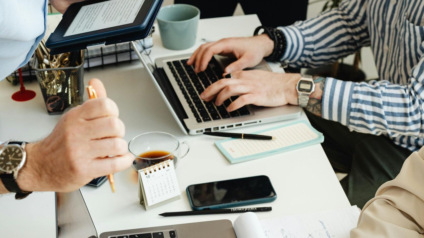 Consulting Beratungsszene: mehrere Menschen an einem Schreibtisch mit Laptops und Unterlagen