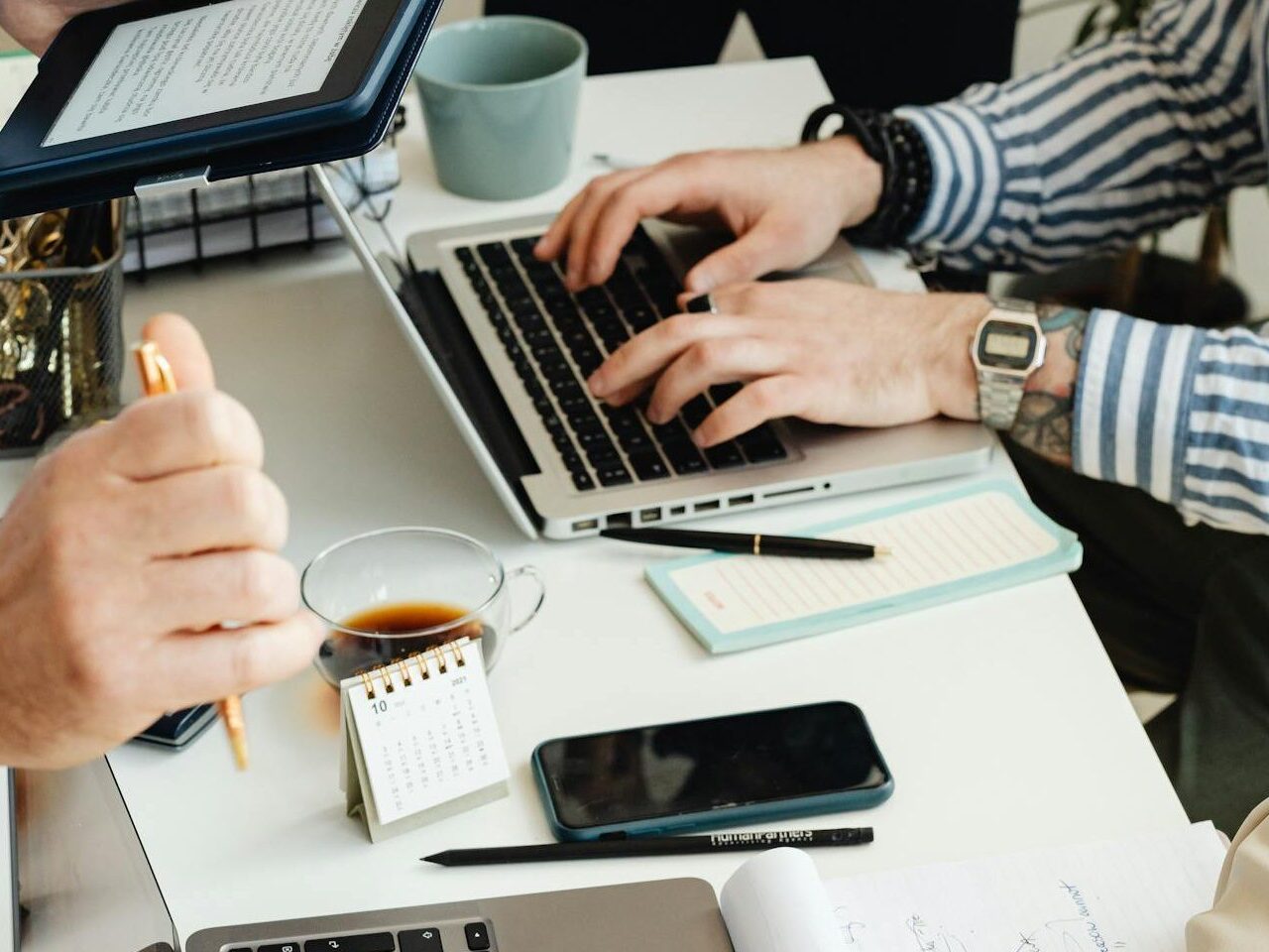 Consulting Beratungsszene: mehrere Menschen an einem Schreibtisch mit Laptops und Unterlagen